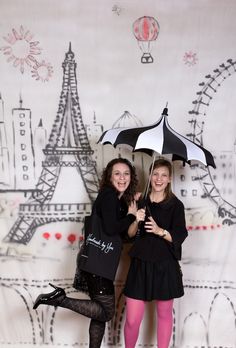 two women standing next to each other with umbrellas in front of the eiffel tower