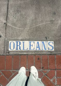 a person standing on the sidewalk with their feet up in front of an orleans street sign