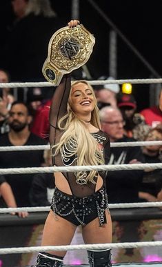 a woman holding up a wrestling belt in front of a crowd