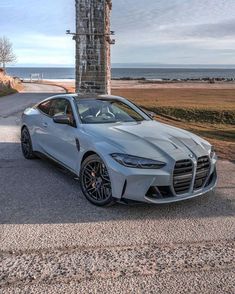 a silver sports car is parked on the side of the road next to an ocean