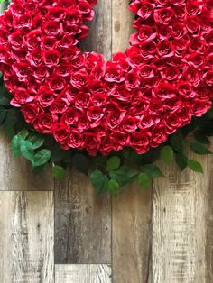 red roses arranged in the shape of a heart on a wooden background with green leaves