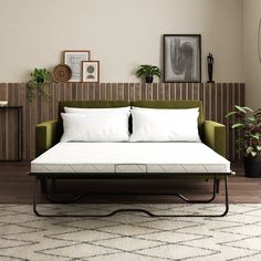 a green couch with white pillows on it in a living room next to a plant