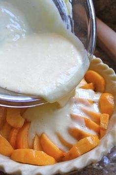 a spoon is being used to scoop some fruit into a pie dish with cream on top