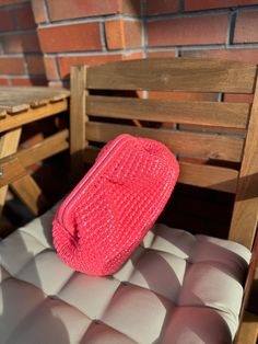 a pink purse sitting on top of a wooden chair next to a brick wall and table