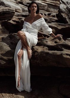 a woman in a white dress standing on rocks with her legs spread out and one leg bent