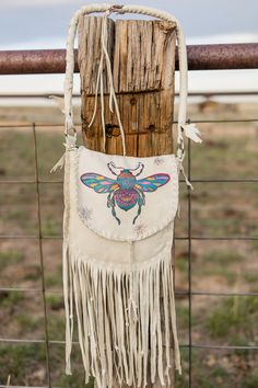 This little beauty is made from Wyoming hunted and tanned deer leather. Hand stitched lacing and fringe down the bottom of the front of the purse. The queen bee on the front is hand drawn with metallic ink and spray protected from soiling. I made it a scarab bee of sorts. We see all sorts of colorful bugs on the high plains desert. So here is my fantasy scarab queen bee. Purse is lined with 100% cotton batik print in colors to compliment the front flap artwork. Interior pocket.  Purse measures 10 inches by 10 inches by 1.5 inches. The strap has a 16-inch drop. and is round braided and padded.  100% hand constructed by me.  Ready for your adventure. Colorful Bugs, Bee Purse, Spirit Bags, Artwork Interior, Batik Print, Boho Purses, Gold Bag, Hobo Bags, Batik Prints