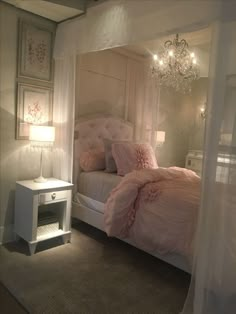 a white bed sitting under a chandelier next to a night stand and table