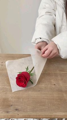 a person is wrapping paper around a rose on top of a wooden table with a white coat