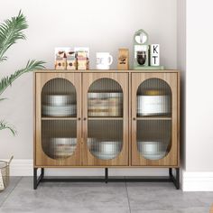 a wooden cabinet with glass doors and metal legs in front of a wall mounted plant