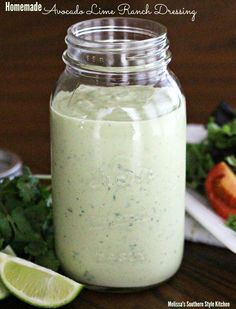 a glass jar filled with dressing next to a salad on a wooden table and lime wedges