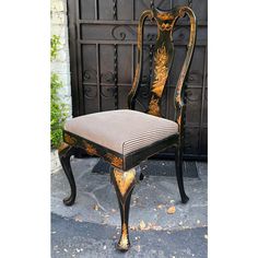 an antique chair with gold and black paint on it's back, sitting in front of a gate