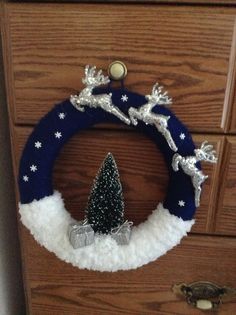 a christmas wreath is hanging on the side of a wooden dresser with silver and white decorations