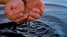 two hands are holding water from a stream