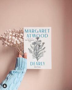 a person's hand holding a book about dearly by margaret atwood