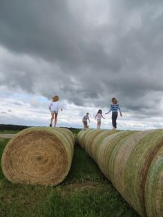 three children are walking on top of hay bales in a field under a cloudy sky