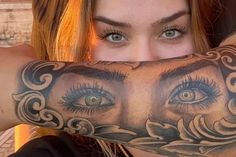 a woman is covering her face with an arm tattoo that has eyes and leaves on it