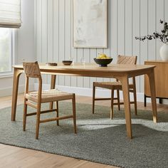 a dining room table with two chairs and a bowl of fruit on the table next to it