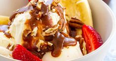 an ice cream sundae with nuts and strawberries in a white bowl on a table