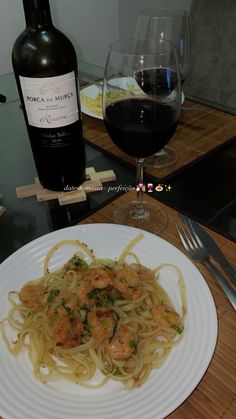 a white plate topped with pasta and shrimp next to a bottle of wine