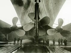 an old black and white photo of men standing in front of a large propeller ship