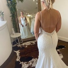 a woman in a white wedding dress looking at herself in the mirror with her back to the camera