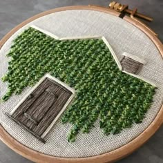 a close up of a cross stitch pattern on a wooden hoop with green grass growing out of it