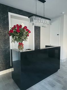 a vase with red roses sitting on top of a black counter next to a chandelier