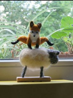 a stuffed animal is sitting on top of a fake sheep in front of a window