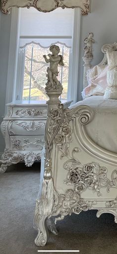 a white bed sitting in a bedroom next to a window with a statue on top of it