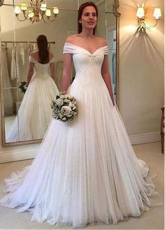 a woman standing in front of a mirror wearing a wedding dress with off the shoulder sleeves