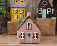 small pink house with green roof and windows on wooden table next to potted plant