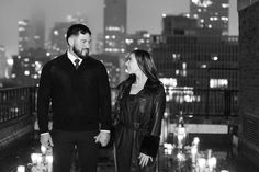 a man and woman holding hands while standing on a roof top with candles in the background