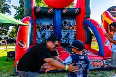 two men standing next to each other near an inflatable bouncer with footballs on it