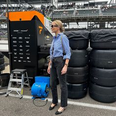 a woman standing in front of tires at a race track with an orange and black machine behind her