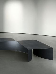 an empty room with two black tables in the center and three white walls behind it