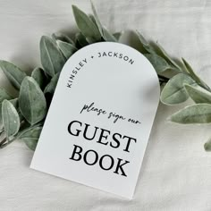 the guest book is next to some green leaves on a white sheet with black lettering