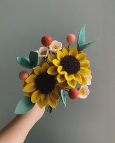 a person's hand holding a paper sunflower bouquet