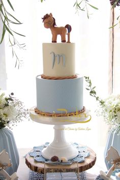 there is a blue and white cake with a horse on top that has the letter m on it