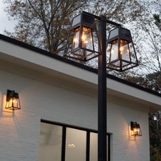 three light fixtures on top of a white brick building with trees in the back ground