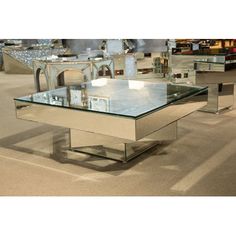 a glass and chrome coffee table on display in a room with other tables behind it