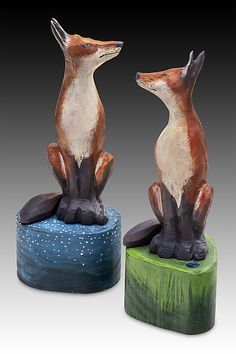 two ceramic figurines of foxes sitting on top of a blue and green base