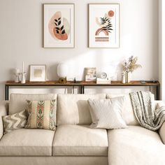 a living room with white couches and art on the wall above them in front of a window