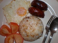 a white plate topped with eggs, rice and sausages next to tomato wedges