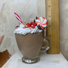 a cup filled with whipped cream and candy canes on top of a table next to a ruler