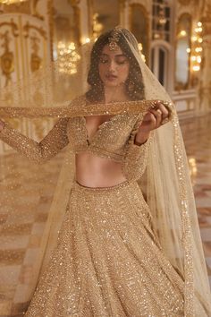 a woman in a gold lehenga and veil is posing for the camera with her hands on her hips