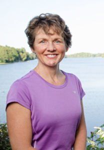 a woman standing in front of a body of water with trees and bushes around her