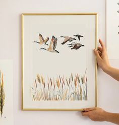 a person holding up a framed painting with birds flying over it