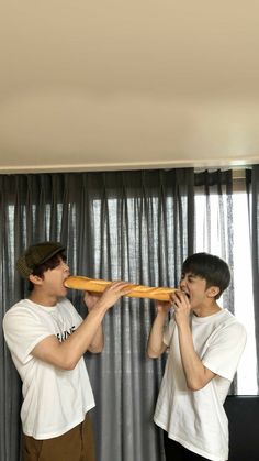 two young men standing next to each other while holding bread in their hands and looking into the distance