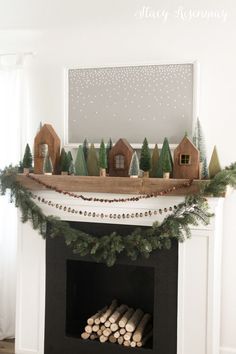 a fireplace decorated for christmas with pine trees and houses on the mantel above it