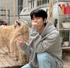 a man sitting on the ground next to a dog in a cage